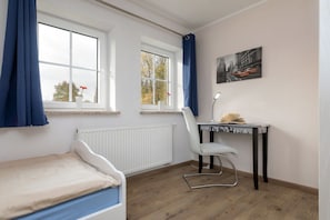 A room with a bed, a desk with a chair, a radiator, and a window with curtains. - Holiday home in Zingst with Wi-Fi and parking (Zingst)
