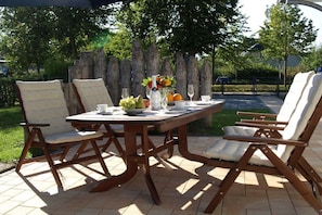 Un espace de restauration en plein air avec une table et des chaises en bois, un vase rempli de fleurs et un saladier de fruits.