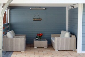 A covered outdoor seating area with two wicker sofas, a small table with a bottle and flowers, and a wall-mounted light fixture. - Holiday home in Zingst with Wi-Fi and parking (Zingst)