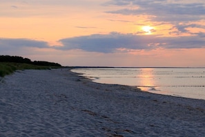 Une plage au coucher du soleil, avec une eau calme et une côte lointaine.
