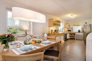 A modern kitchen with wooden cabinets, a dining table set for four, and a large pendant light. - Holiday home in Zingst with Wi-Fi and parking (Zingst)