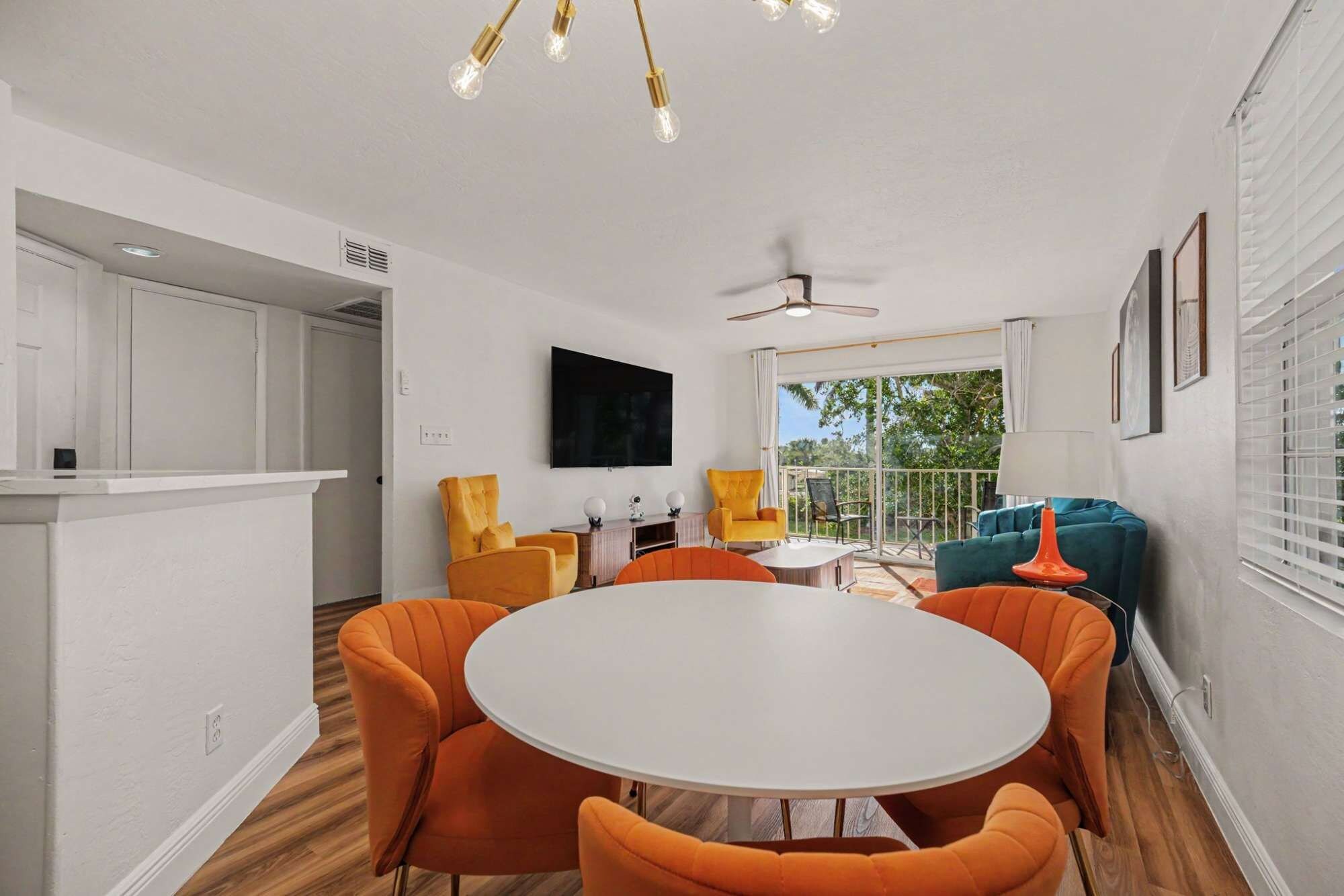 Un coin repas avec une table ronde et des chaises orange, un téléviseur fixé au mur et un ventilateur de plafond.