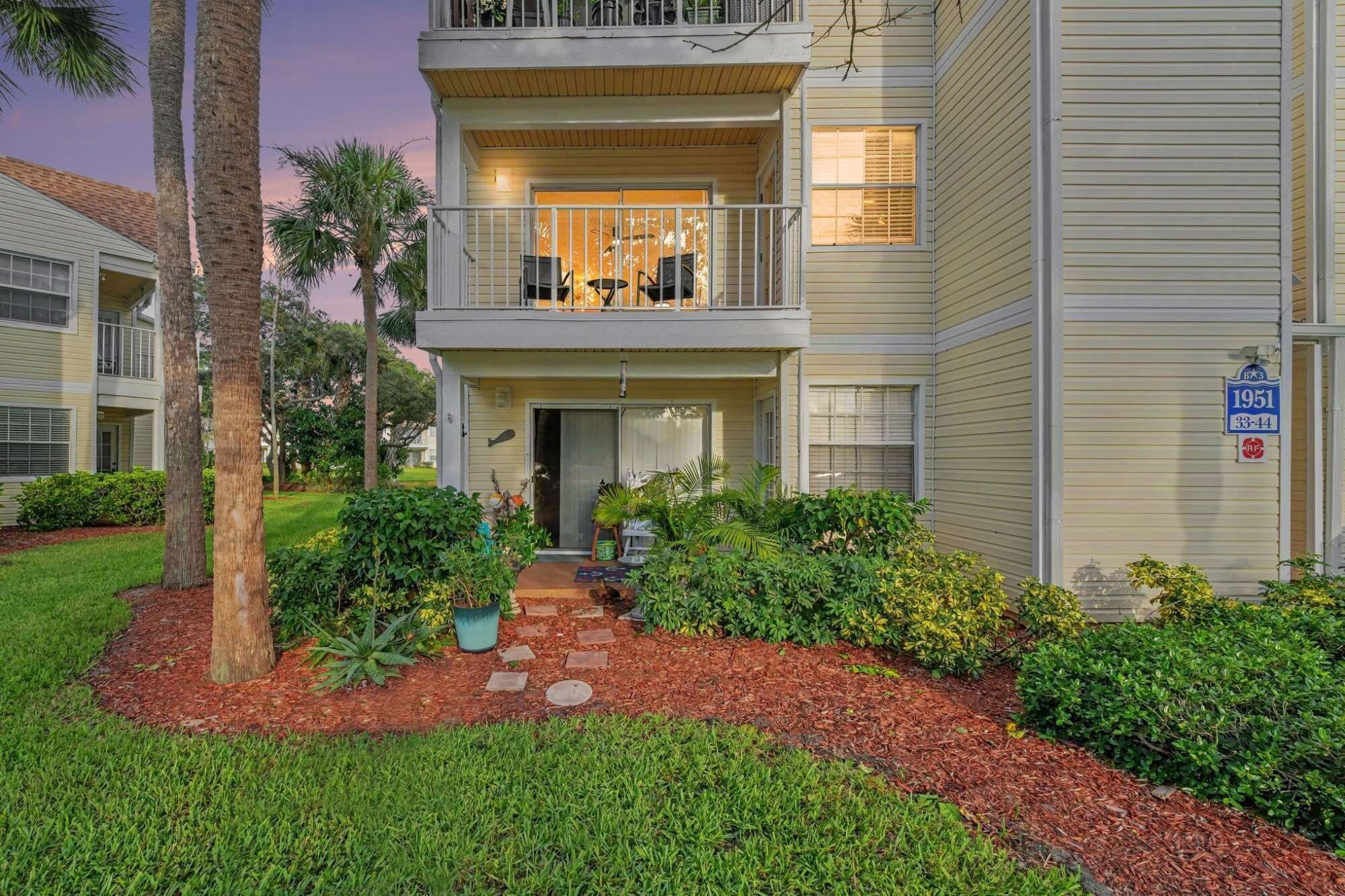 A two-story residential building with a balcony, a driveway, and a well-maintained garden.