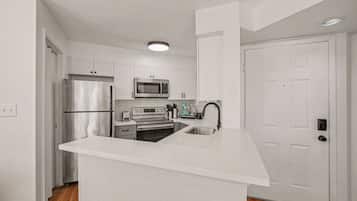 A modern kitchen with white cabinetry, a stainless steel refrigerator, a microwave, an oven, and a sink.