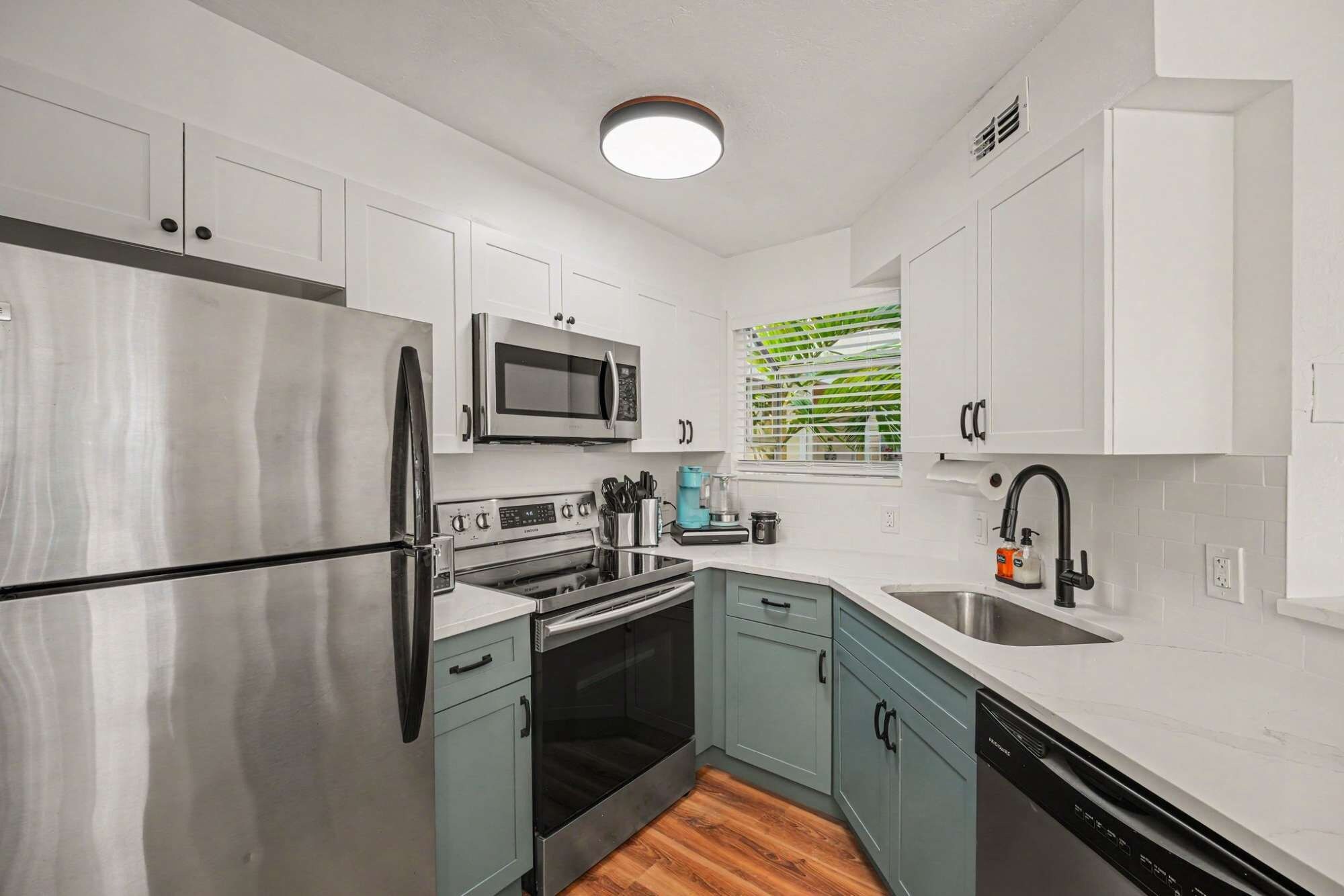 A compact kitchen with a stainless steel refrigerator, a microwave, an oven, a dishwasher, and a sink.