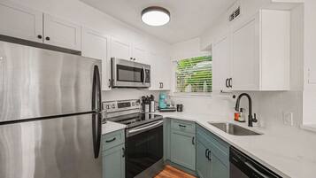A compact kitchen with a stainless steel refrigerator, a microwave, an oven, a dishwasher, and a sink.