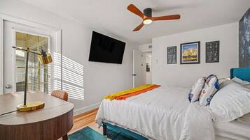 A bedroom with a bed, a desk, a ceiling fan, and a window with blinds.