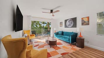 A living room with a sofa, armchairs, a coffee table, a ceiling fan, and artwork on the walls.