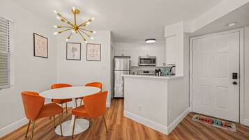 A modern kitchen with white cabinets, a stainless steel refrigerator, a microwave, and a coffee machine.
