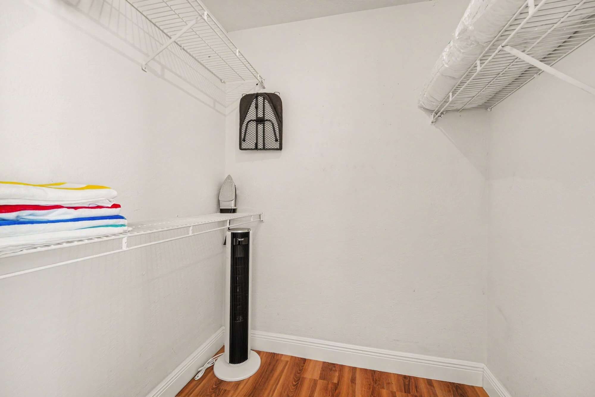 A corner of a room with a white wall, a wooden floor, a white radiator, and a shelf with folded clothes.