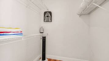 A corner of a room with a white wall, a wooden floor, a white radiator, and a shelf with folded clothes.
