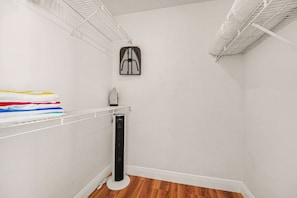A corner of a room with a white wall, a wooden floor, a white radiator, and a shelf with folded clothes. - Space Age King Bed Condo · Half Mile to Beach (Melbourne)