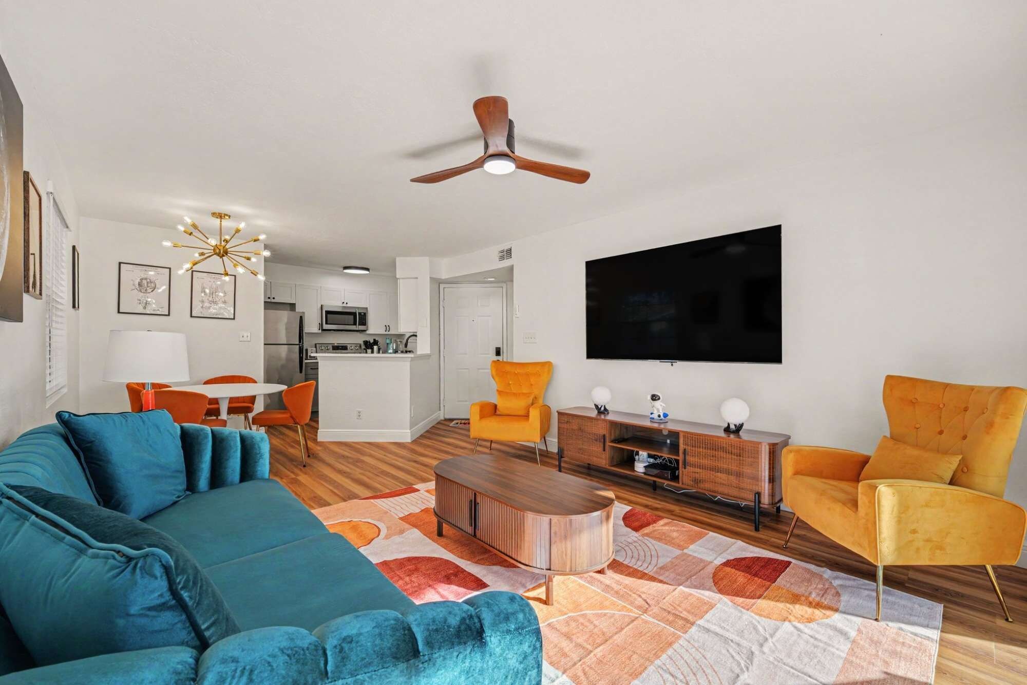 A modern living room with a sofa, chairs, a coffee table, a TV, and a ceiling fan.