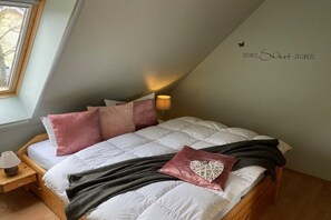 Ein Schlafzimmer mit schrägverdachter Decke, einem Bett mit vielen Kissen, einer Nachttischlampe und einem Wandschild mit der Aufschrift 'HOME Sweet HOME'.