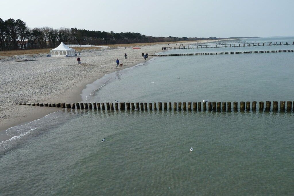 Une plage avec une tente blanche, une jetée en bois et un rivage sablonneux.