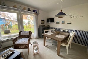 Ein Essbereich mit Tisch und Stühlen, ein Korbstuhl, eine Laterne und ein Fernseher an der Wand.