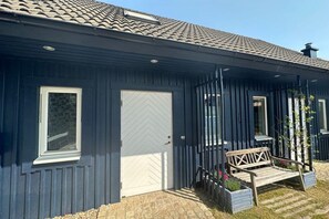 Ein Haus mit dunkler Außenfassade, einer weißen Tür und einer kleinen Veranda mit einer Bank.