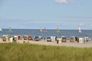 A beach with multiple beach huts and a row of sailboats on the water. - Holiday apartment with 2 bedrooms (Heiligenhafen)