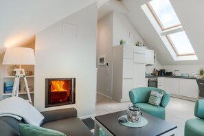 A modern living room with a fireplace, a dining area, and a kitchen with skylights. - Holiday apartment with 2 bedrooms (Heiligenhafen)