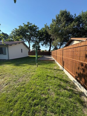 A backyard with a wooden fence, a small shed, and a tree. - Villa du Betey 4 étoiles 8pers climatisée Andernos les bains (Andernos-les-Bains)