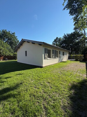 A single-story building with a flat roof, a small porch with a railing, and a grassy yard. - Villa du Betey 4 étoiles 8pers climatisée Andernos les bains (Andernos-les-Bains)