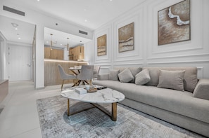 A modern living room with a sofa, a coffee table, and a dining area with chairs. - Seven Palm | 1BR, Sweet, Stylish & Serene (Dubai)