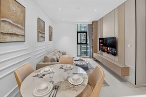 A modern dining area with a marble table set for four, a sofa with cushions, and a large flat-screen TV mounted on the wall. - Seven Palm | 1BR, Sweet, Stylish & Serene (Dubai)