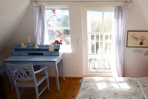 Une chambre à coucher avec un lit, un bureau et une chaise. Il y a une fenêtre avec des rideaux et un tableau encadré au mur.