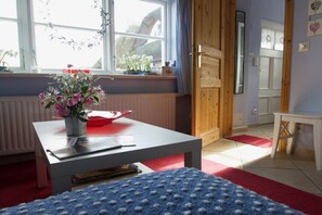 Ein Zimmer mit Fenster, einem Tisch mit Blumenvase, einer Heizung und einer Tür.