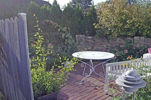 Ein Garten-Pavillon mit einem runden Tisch und weißen Stühlen, umgeben von Kübelpflanzen und einer Steinmauer.