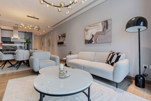A modern living room with a sofa, chairs, a coffee table, and a floor lamp. - Dere Residences - 108 (Dubai)