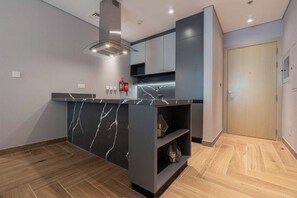 A modern kitchen with a marble countertop, built-in cabinets, a stainless steel range hood, and a wooden floor. - Dere Residences - 108 (Dubai)