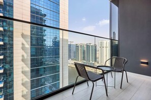 A modern balcony with two chairs, a glass railing, and a view of high-rise buildings. - Trillionaire | 1BR, Trendy, Timeless & Tempting (Dubai)