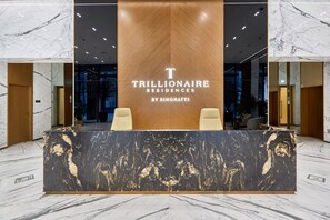 A reception desk with a marble top, two chairs, and a wooden panel with the text 'TRILLIONAIRE RESIDENCES BY BINGHATTI'. - Trillionaire | 1BR, Trendy, Timeless & Tempting (Dubai)