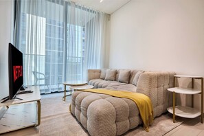 A modern living room with a sectional sofa, a coffee table, a TV, and a small side table. - Trillionaire | 1BR, Trendy, Timeless & Tempting (Dubai)