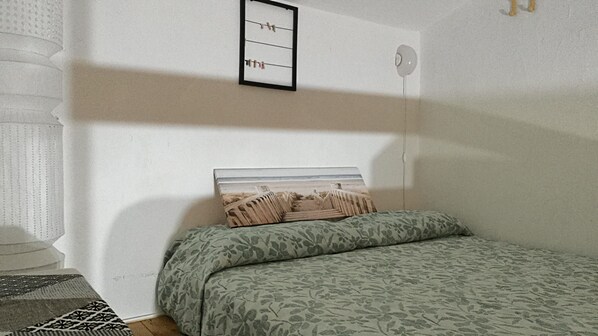 Quarto com cama, prateleira na parede com roupas e janela.