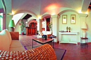 Ein geräumiger Wohnbereich mit Sofa, Sesseln, einem Couchtisch und einem Kamin. Übertöpfe und eine Lampe stehen auf einem Beistelltisch.