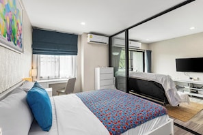 A modern hotel room with a bed, a desk, a chair, a television, and a large window. - Bright Corner 1 Bed Retreat (TC-F306) (Thalang)