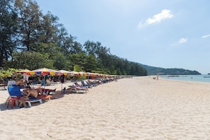 Ein Strand mit Reihen von Liegestühlen und Sonnenschirmen, einem klaren Himmel und einem ruhigen Meer.