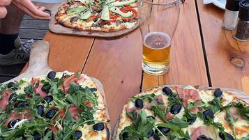 Two pizzas on a wooden table with a glass of beer and salt and pepper shakers.