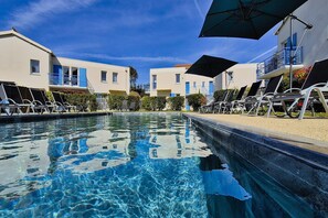 A swimming pool with lounge chairs and umbrellas, surrounded by buildings with balconies. - Connected Coastal Duo for Groups (Saint-Palais-sur-Mer)