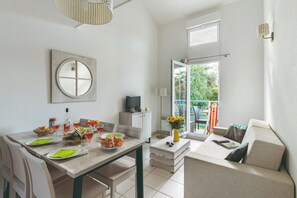 A modern kitchen with a dining table set for a meal, a television, and a view of the outdoors. - Connected Coastal Duo for Groups (Saint-Palais-sur-Mer)