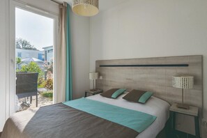 Ein Schlafzimmer mit einem Bett, zwei Nachttischen, einem Fenster mit Vorhängen und Blick ins Freie.