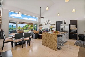 Une cuisine moderne dotée d’un îlot central, de tabourets de bar et d’un coin repas offrant une vue sur l’extérieur.