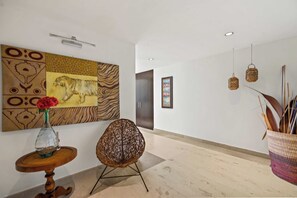 Una hall con un grande quadro astratto, una poltrona in vimini, un vaso con fiori e un cesto appeso con piante.