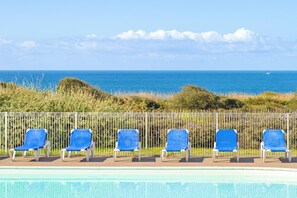 A poolside area with six blue chairs and a metal fence, overlooking a clear blue sea. - Oceanfront Suite for Five (Les Sables-d'Olonne)
