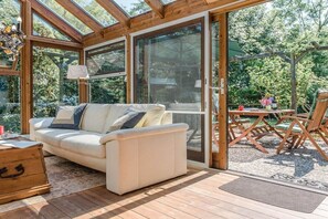 A sunlit room with a sofa, a wooden table, and a glass door leading outside. - Farmhouse by the sea || Langballig (Langballig)
