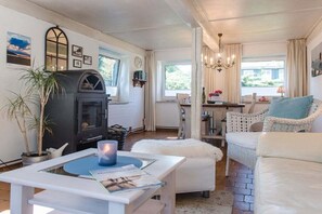 Una sala de estar acogedora con chimenea, muebles blancos y un comedor con mesa y sillas.