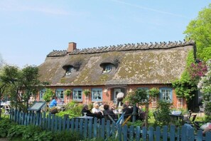 A traditional thatched-roof building with a picket fence, outdoor seating, and a garden. - Farmhouse by the sea || Langballig (Langballig)