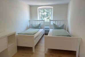 A bedroom with two single beds, a white dresser, and a window with a view of trees. - Holiday apartment with 2 bedrooms (Stoltebüll)